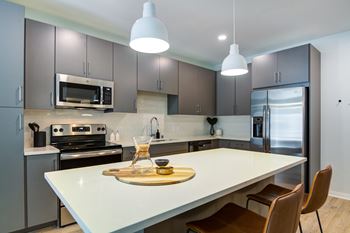 A modern kitchen with a white island and brown chairs.